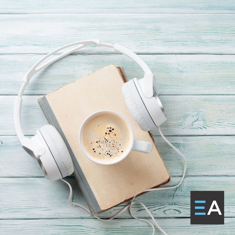 Over-the-ear headphones placed around a beige book with a cup of coffee on it