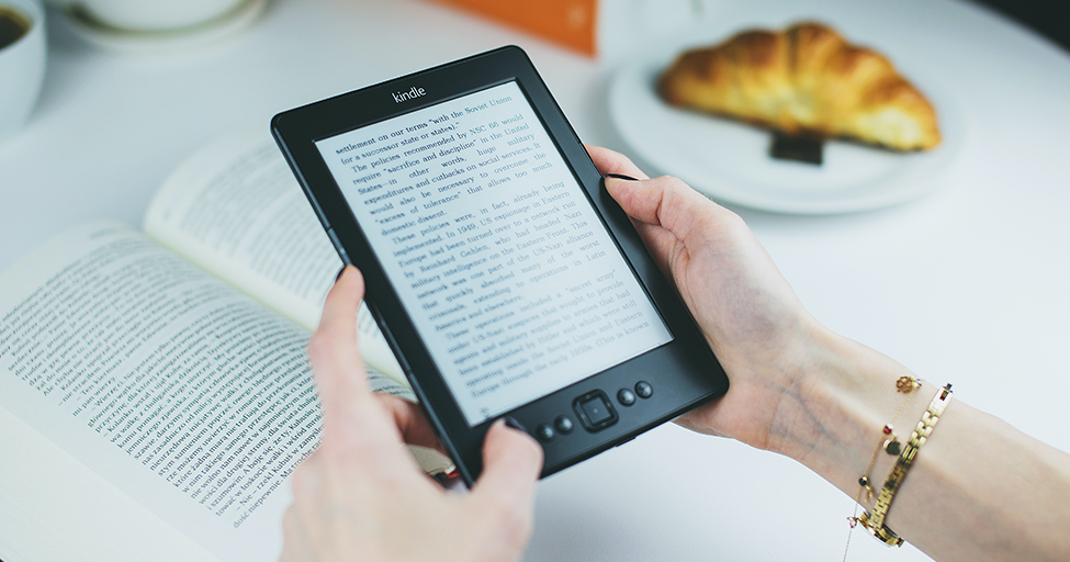 hands holding an e-book over a physical book
